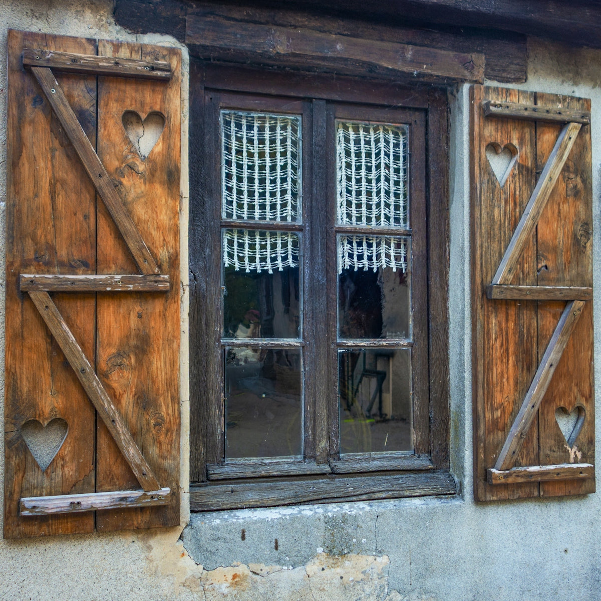 Rustic wooden shutters frame a window with curtains.